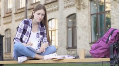 Yorgun genç kadın bankta oturan ve (freelancing) okuyor. Kağıt deftere yazmak, hayal kırıklığına uğradım. kağıt buruşturulmuş ve atma.