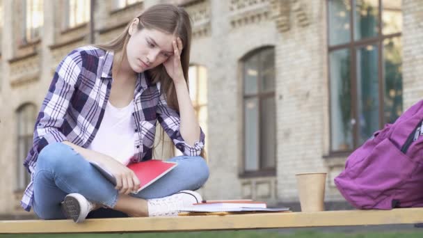 紧张和愤怒的年轻女子坐在长凳上 看着一边 然后把纸笔记本和课本扔在地上 — 图库视频影像