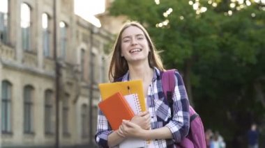 Mutlu, gülümseyen genç kadın kitaplar la tutarak nad ders kitapları, sokakta yürüyor. El çekimi.