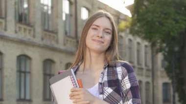 Üniversite yakınında çekici genç öğrenci kız yakın portresi. Gülümsüyor, mutlu ve kameraya bakıyor. El çekimi.