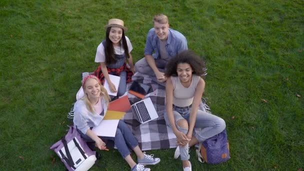 Grupp Studenter Som Sitter Gräset Tittar Kameran Och Gör Bye — Stockvideo