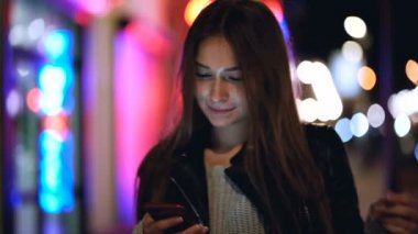 Akşam caddesinde Wirth akıllı telefonuyla duran mutlu beyaz kadın portresi. Biraz dans, iyi bir ruh hali. Akıllı telefonlara bakıyorum. Yavaş çekim.