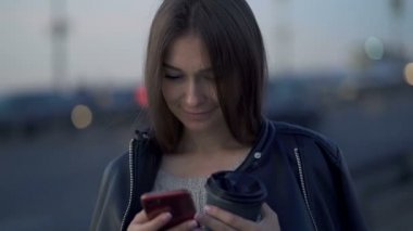 Sokakta elinde akıllı telefonuyla duran genç beyaz bir kadın. Mesaj atmak, internette arama yapmak. El kamerasıyla. Yavaş çekim.