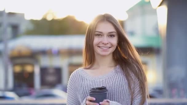 微笑的年轻女子走在街上 举着咖啡杯 看着相机 慢动作 手持射击 — 图库视频影像