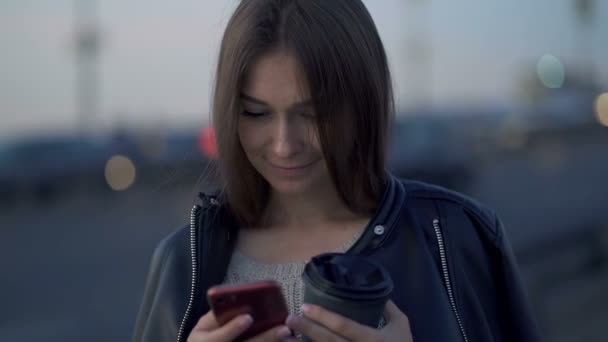 年轻的高加索女人手里拿着智能手机站在街上 发短信 上网搜索 手持射击 慢动作 — 图库视频影像