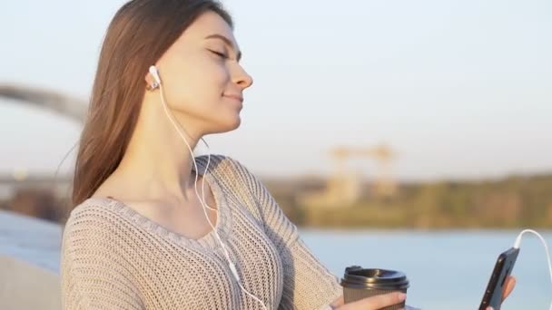 Νεαρή Γυναίκα Που Ακούει Μουσική Στα Ακουστικά Έξω Και Πίνει — Αρχείο Βίντεο