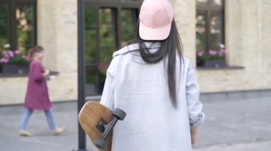 Genç bir kadın kaykayla yürüyor. Arkadan görüntüle.