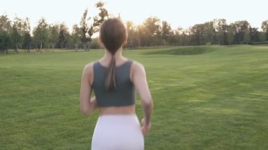 Parkta koşan genç bir kadın. Arkadan bak. Yavaş çekim.