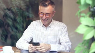 Kahve dükkanında cep telefonuyla oturan gülümseyen adam. Yavaş çekim.