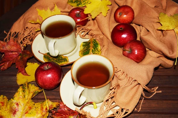 two warming tea apples and autumn leaves on a wooden balcony table