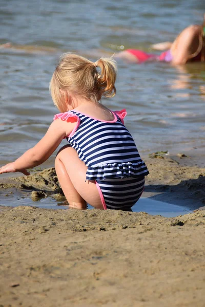 Niña en la orilla del lago está jugando con la arena — Foto de Stock