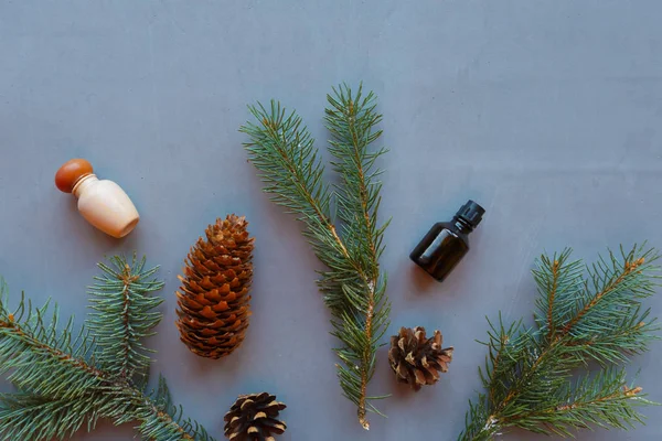 Cosmetic bottles and coniferous branches and cones on gray background. Natural cosmetic product concept