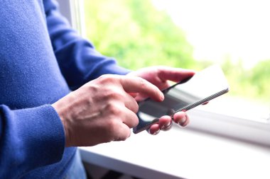 Pencerenin yanında cep telefonu kullanan bir adama yaklaş