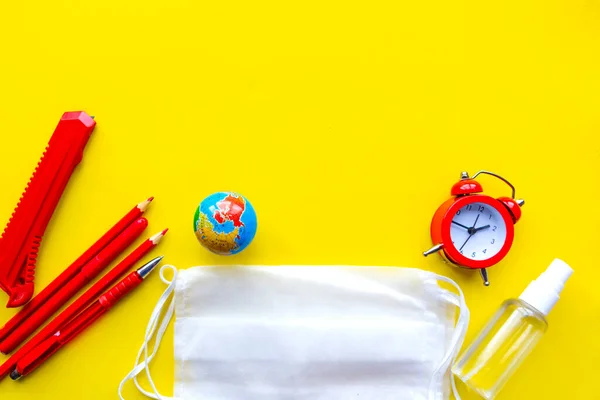 School supplies, medical mask and hand sanitizer on bright yellow background, copy space for the text. School quarantine concept