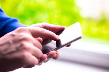 Pencerenin yanında cep telefonu kullanan bir adama yaklaş