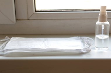 Pencere kenarında tıbbi maske ve el dezenfektanı var. Evde kalın covid-19 konsepti