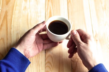 Erkeğin elleri arka planda kahve fincanı tutuyor.