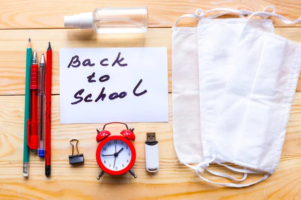 School supplies, medical mask and card with message Back to School on wooden background. School quarantine concept