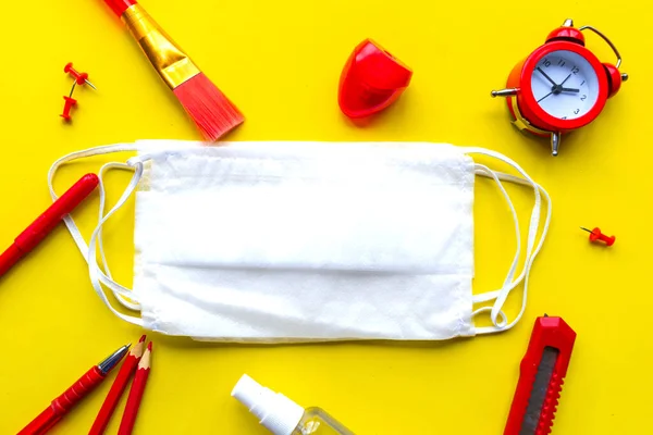 School supplies and medical mask on bright yellow background. School quarantine concept