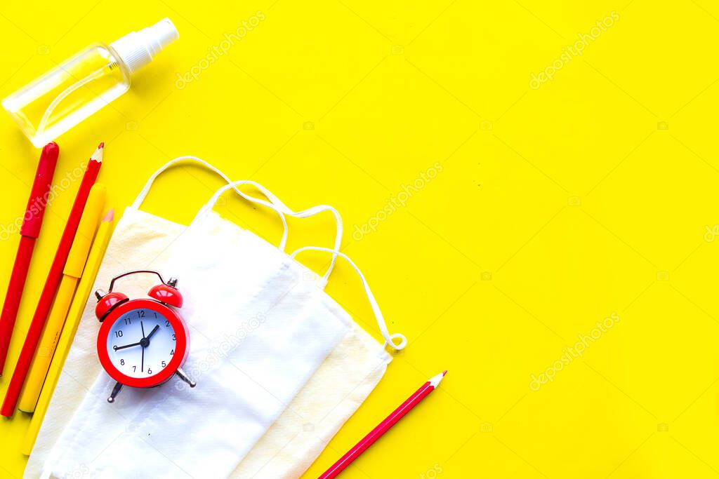 Alarm clock, pencils and medical mask on bright yellow background, copy space for the text. Back  to school concept