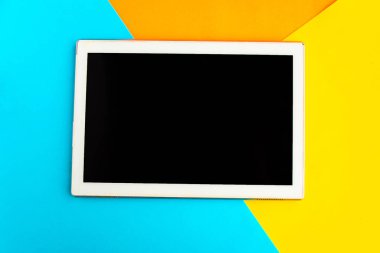 Geometrik mavi, turuncu ve sarı arka planda siyah model ekranlı tablet. Metin için alanı kopyala. Asgari konsept