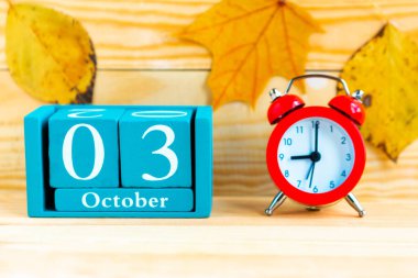 3 Ekim. Ahşap zemin üzerinde ay, tarih ve alarm saati olan mavi küp takvimi.