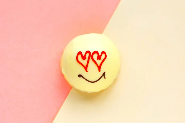 Tasty sweet cake with draw face and heart eyes on geometric pastel pink and yellow  background, top view. Love concept