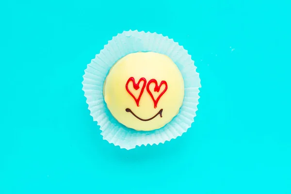 Tasty sweet cake with draw face and heart eyes on bright blue background, top view. Love concept