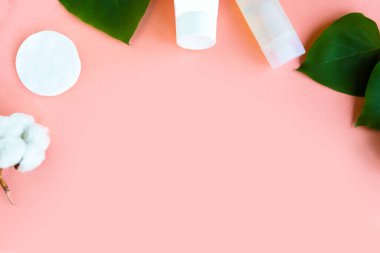 Pamuk çiçekli beyaz kozmetik şişeler ve pembe arka plan manzaralı yeşil yapraklar düz yerde yatıyordu. Doğal organik güzellik ürünü konsepti, Minimalizm tarzı.