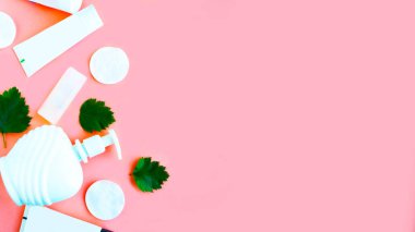 Pembe arka plan manzaralı yeşil yapraklı beyaz kozmetik şişe kapları düz yatıyordu. Doğal organik güzellik ürünü konsepti, Minimalizm tarzı.