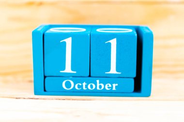 11 Ekim. Ahşap zemin üzerinde ay ve tarih olan mavi küp takvimi.