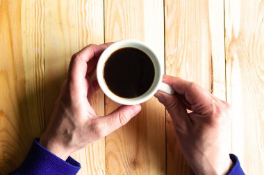 Erkek adam kahve fincanını ahşap arka planda tutuyor.