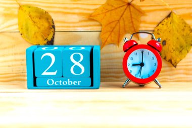28 Ekim 'de. Ahşap zemin üzerinde ay, tarih ve alarm saati olan mavi küp takvimi.