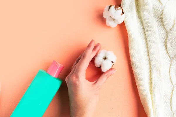 Eco cleaning concept. Washing conditioner, knitted wool sweater and cotton flowers on pink background. Flat lay top view. Bio organic product