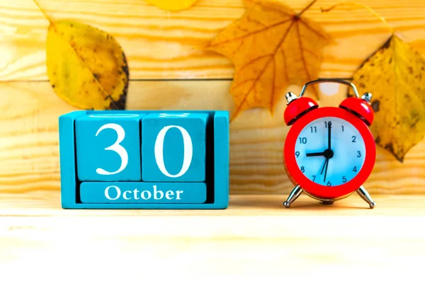 October 30. Blue cube calendar with month and date and alarm clock on wooden background.