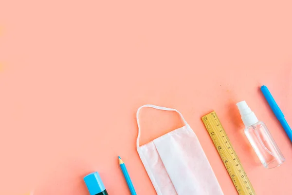 School supplies, medical mask and hand sanitizer on pastel pink background, top view copy space. Back to school concept. School quarantine concept