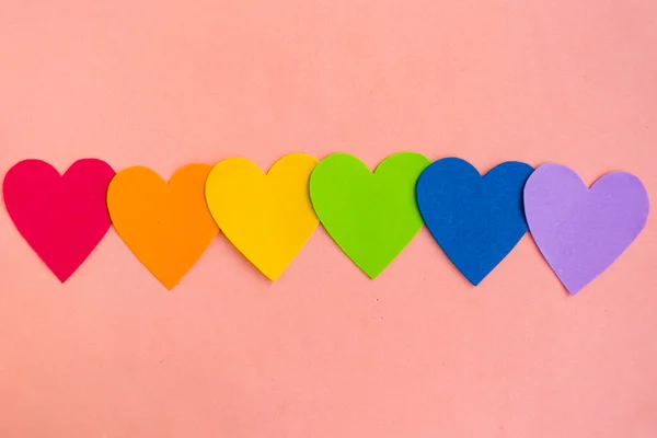 Hearts in lgbtq colors on pastel pink background, top view