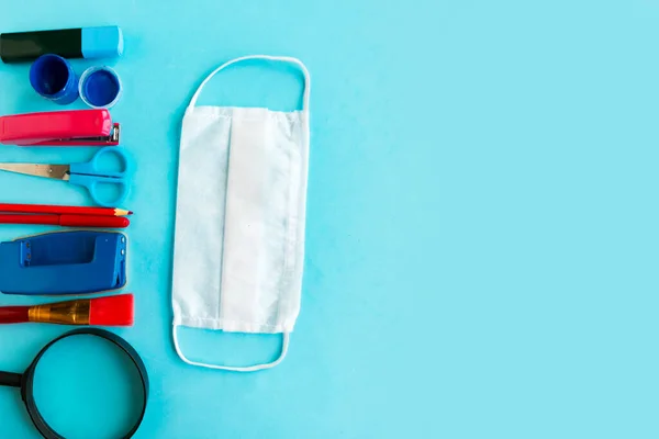 School supplies and medical mask on blue background, top view. School quarantine concept