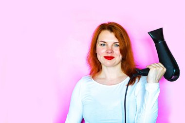 Pembe arka planda saç kurutma makinesi olan bir kızın portresi.