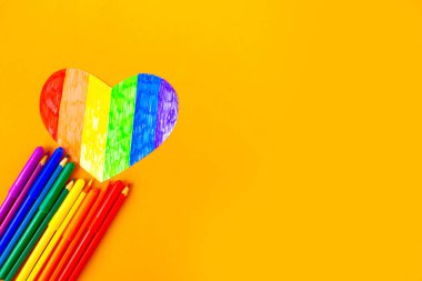 turuncu arkaplanda lgbtq renklerinde kalp ve renkli kalemler, üst görünüm
