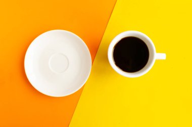 Geometrik turuncu ve sarı arka planda beyaz tabak ve kahve fincanı, üst manzara. Asgari konsept