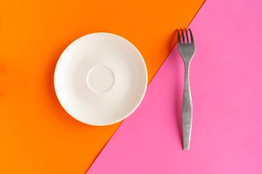 Turuncu ve pembe geometrik arka planda beyaz model plaka ve çatal. Metin için alanı kopyala. Asgari konsept