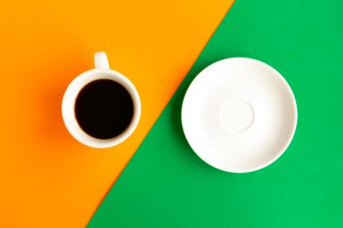 Geometrik turuncu ve yeşil arka planda beyaz tabak ve kahve fincanı, üst manzara. Asgari konsept