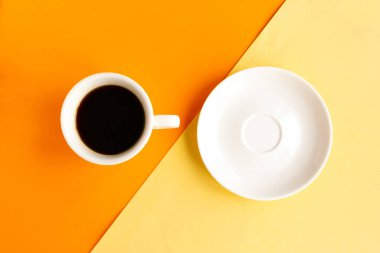 Geometrik turuncu ve sarı arka planda beyaz tabak ve kahve fincanı, üst manzara. Asgari konsept