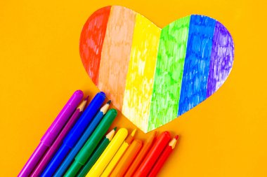 Turuncu arkaplanda lgbtq renklerinde kalp ve kalemler, üst görünüm, boşluk kopyala