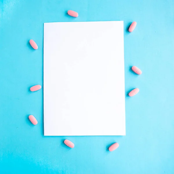 Medical pills and white mockup blank on blue background, top view