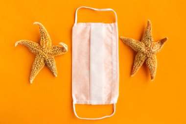 Turuncu arka planda yıldızbalıkları ve tıbbi maske. Coronavirus seyahat kavramı