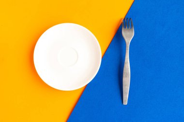 Turuncu ve mavi arka planda boş tabak ve çatal. Metin için alanı kopyala. Asgari konsept