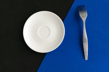 Mavi ve siyah arka planda boş tabak ve çatal. Metin için alanı kopyala. Asgari konsept