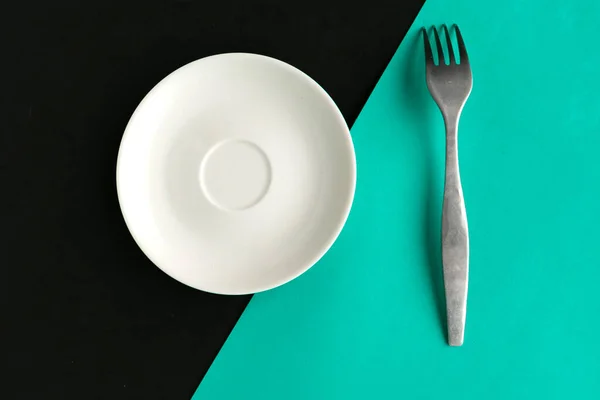 Empty plate and fork on turquoise and black background. Copy space for the text. Minimal concept